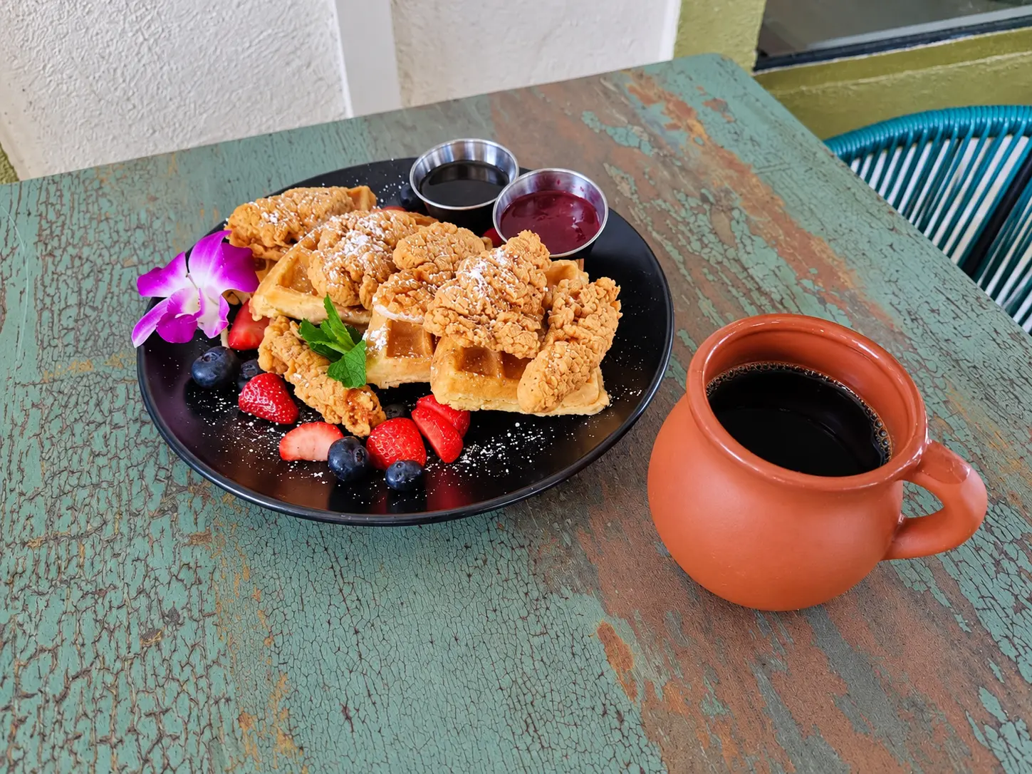 Chicken and waffles with fresh berries and a clay mug of coffee